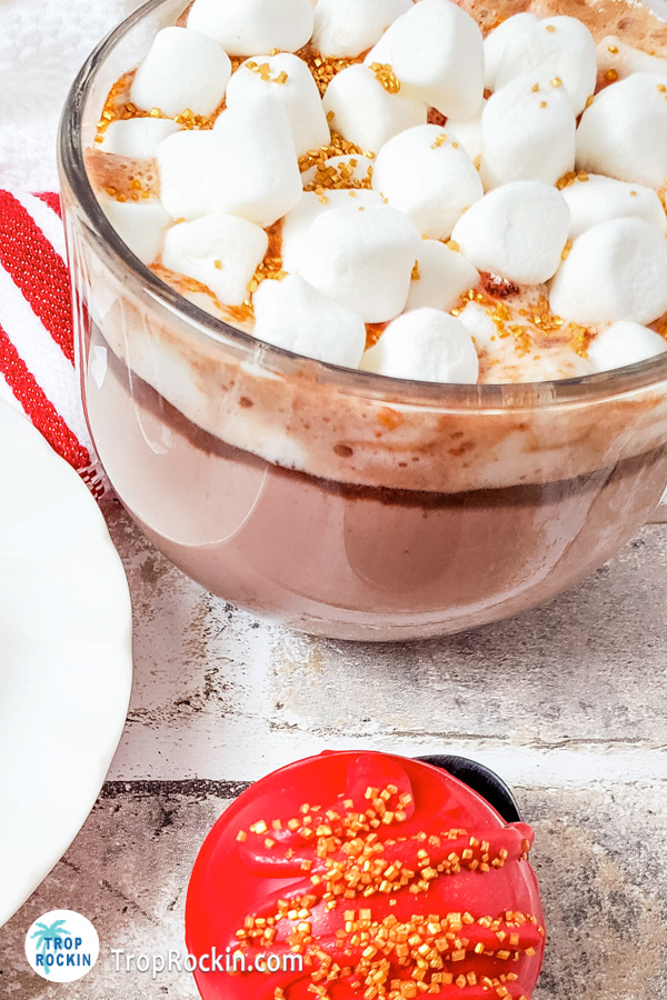 Mug of hot chocolate with marshmallows and a Christmas hot chocolate bomb next to the mug.