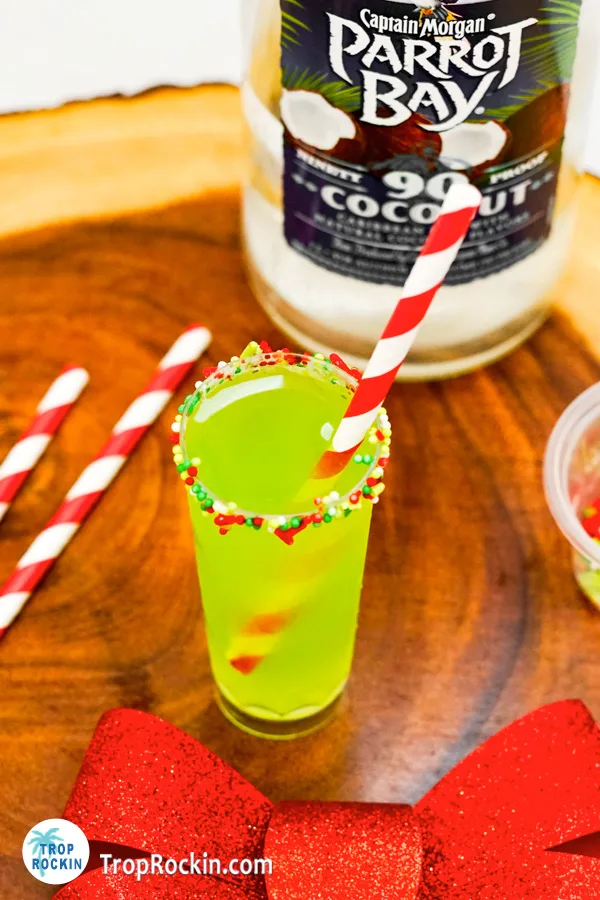Green Christmas shot with sprinkles and straw with a bottle of coconut rum in the background. 