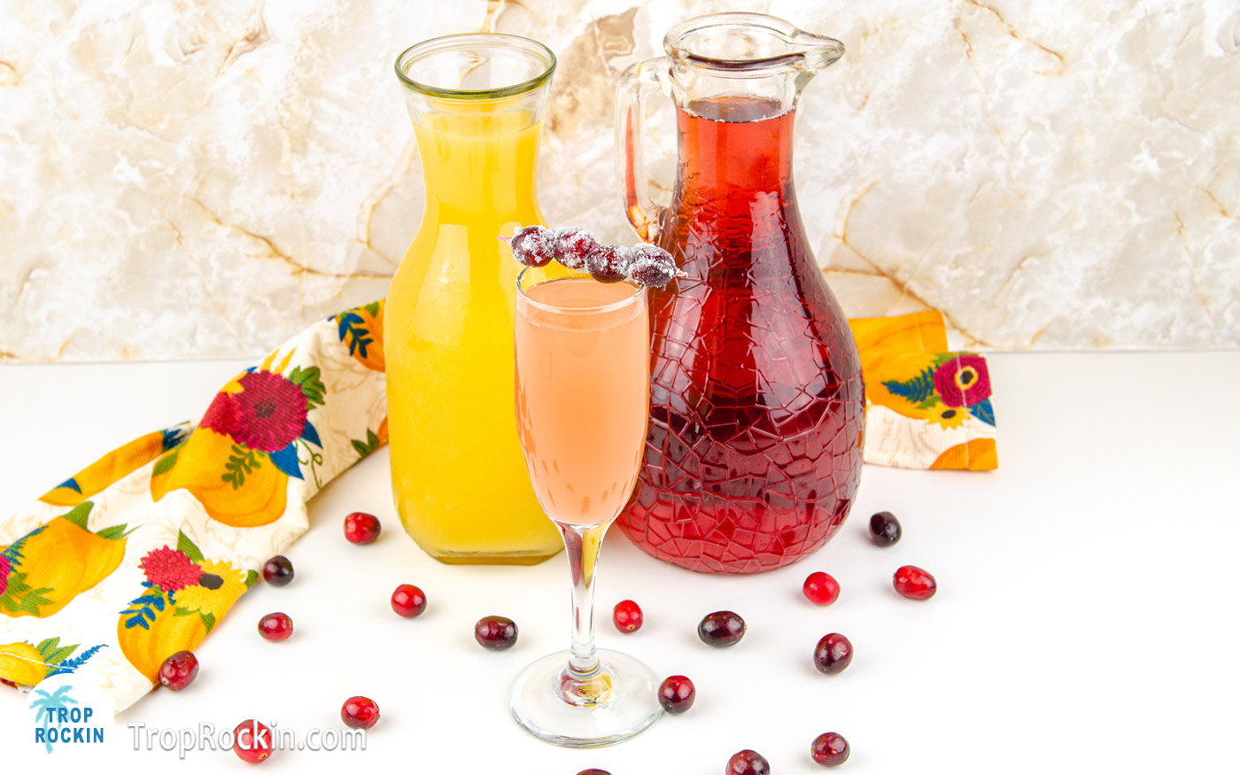 Cranberry Orange Mimosa with a caraft of Orange Juce and a pitcher of Cranberry Juice.