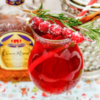 Cranberry Rosemary Cocktail garnished with fresh cranberries and sprig of rosemary with bottle of Crown Royal Whisky in background.