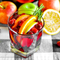 Low ball glass full of fruity cranberry sangria with fresh fruits in the background.