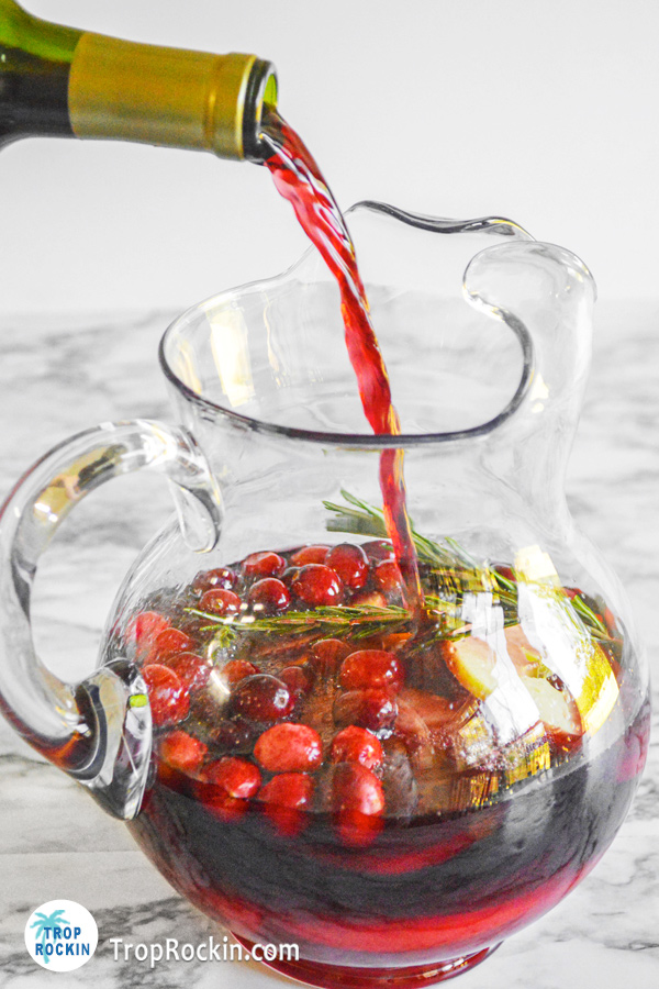 Pouring red wine into a pitcher full of fresh fruits.