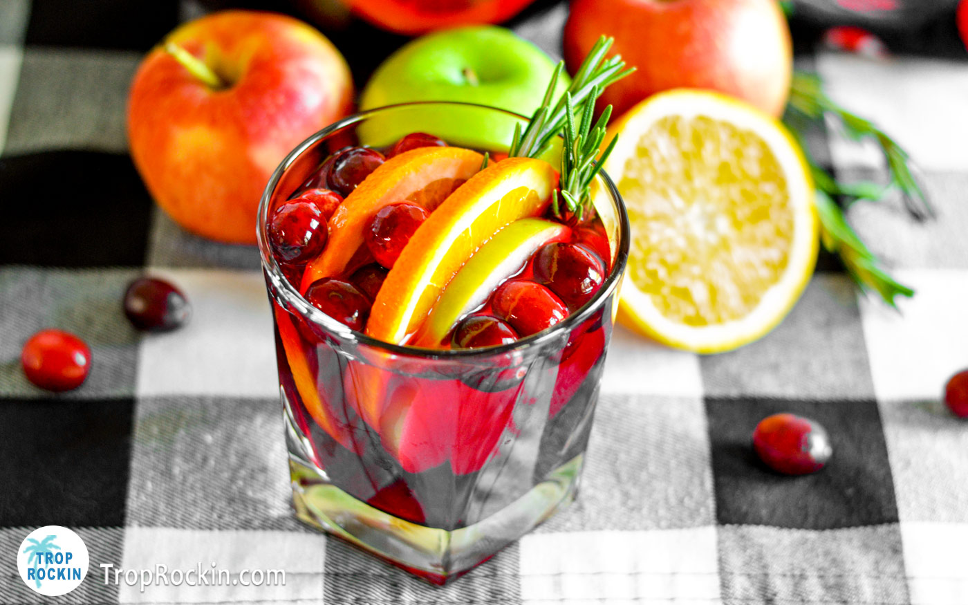 Low ball glass full of fruity cranberry sangria with fresh fruits in the background.