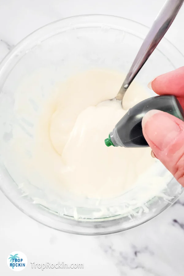 Adding green food coloring to a bowl of melted white chocolate.