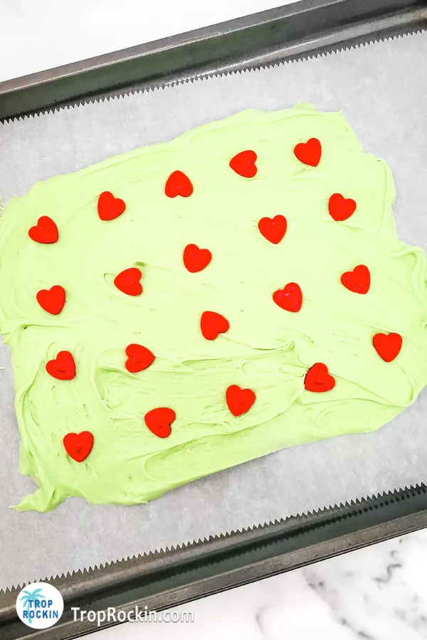 Melted green chocolate on a parchment lined cookie sheet with large red heart sprinkles added on top.