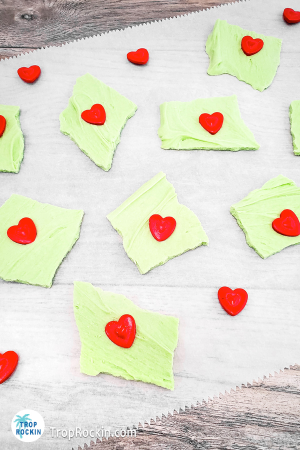 Grinch bark pieces with red heart candy on a piece of parchment paper.