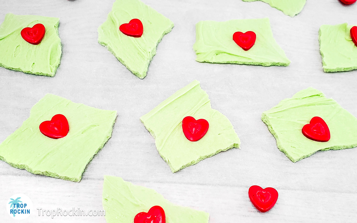 Grinch Bark with red candy sprinkles on top laid out on parchment paper.