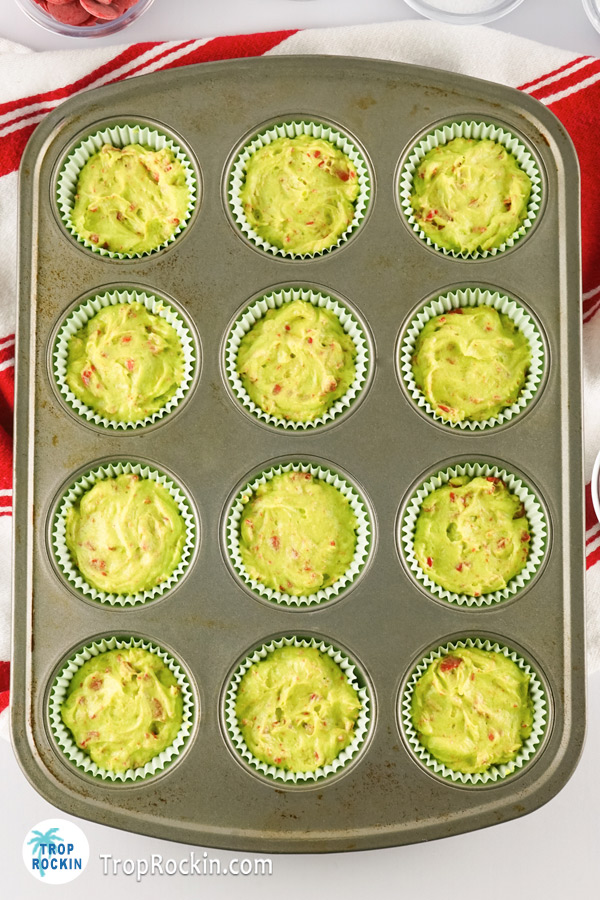 Cupcake tin filled with green cupcake liners and cupcake batter.