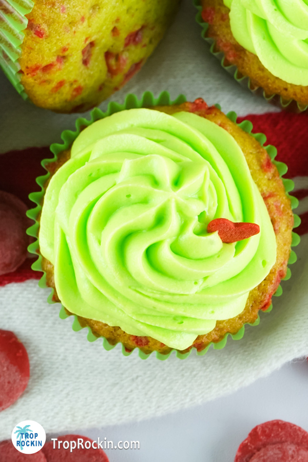 Top view of decorated grinch cupcake showing swirling green frosting on top of the cupcake with a red heart sprinkle of to the right side.
