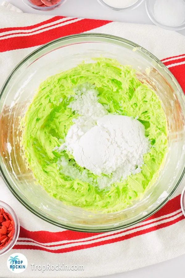 Powder sugar on top of green grinch frosting in mixing bowl.