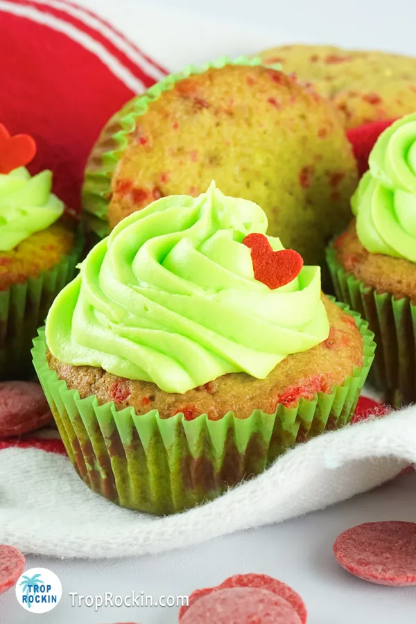 One decorated grinch cupckae with undecorated cupcake in background.