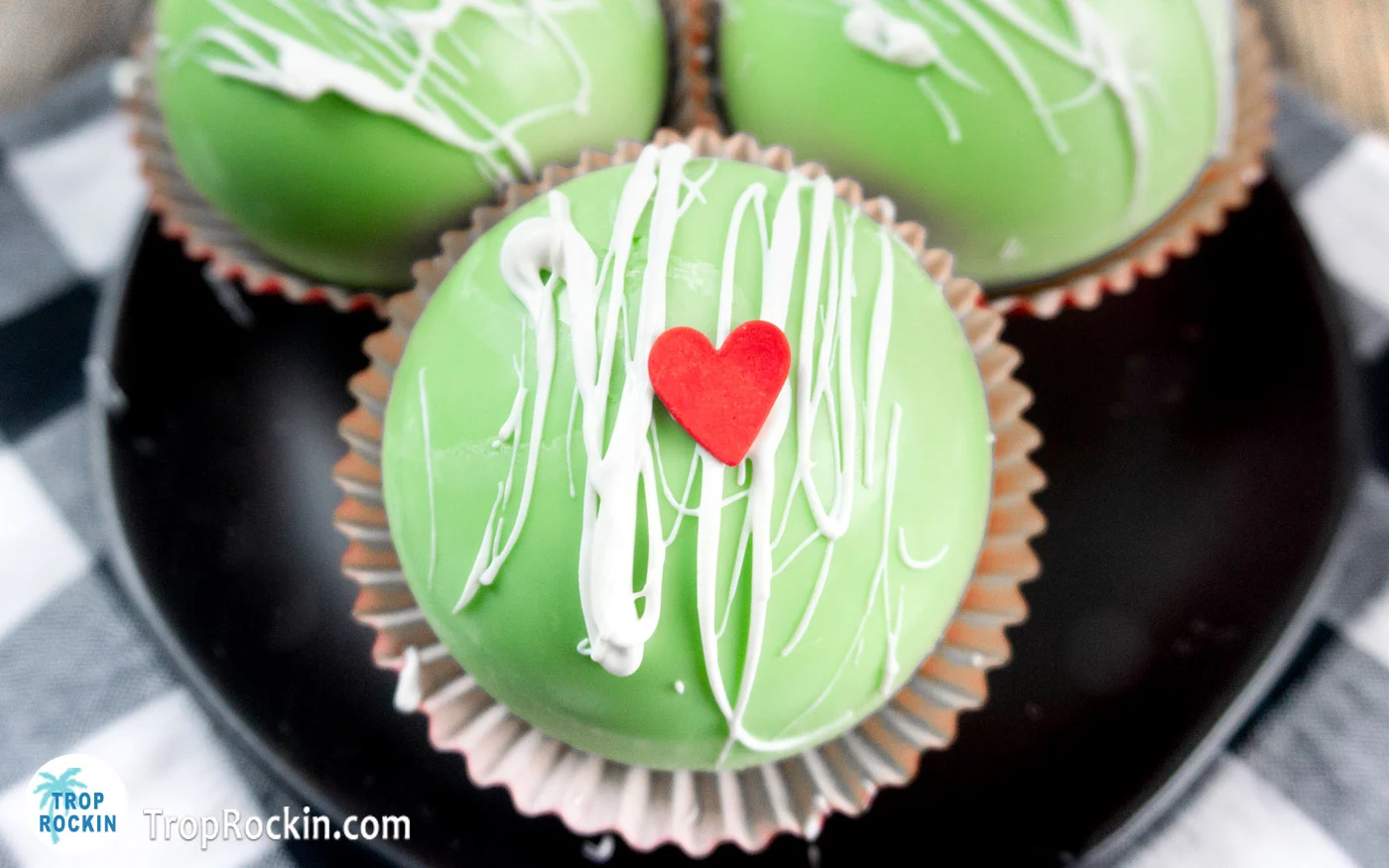 Grinch hot chocolate bomb with white candy drizzle and a red candy heart.