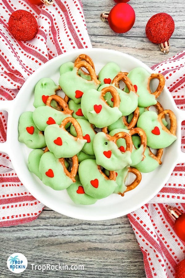 Grinch pretzels piled on a white plate with a red and white kitchen towel underneath the plate.