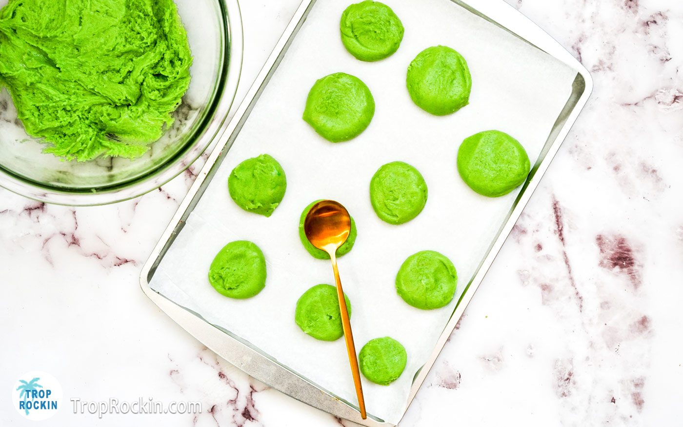 Green sugar cookie dough balls flattened slightly with a spoon on a baking sheet prepared with parchment paper.