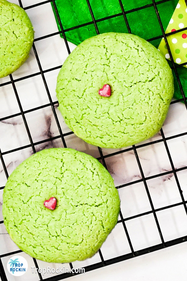Two Grinch Cookies with a red candy sprinkle on top displayed on a wire rack.
