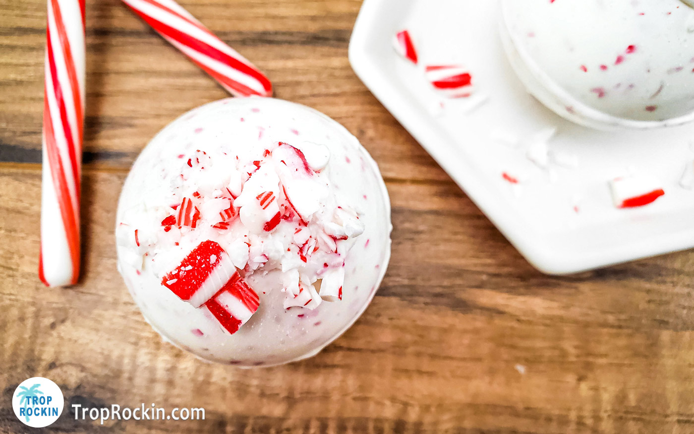 Peppermint hot chocolate bomb on wood background with two candy canes.
