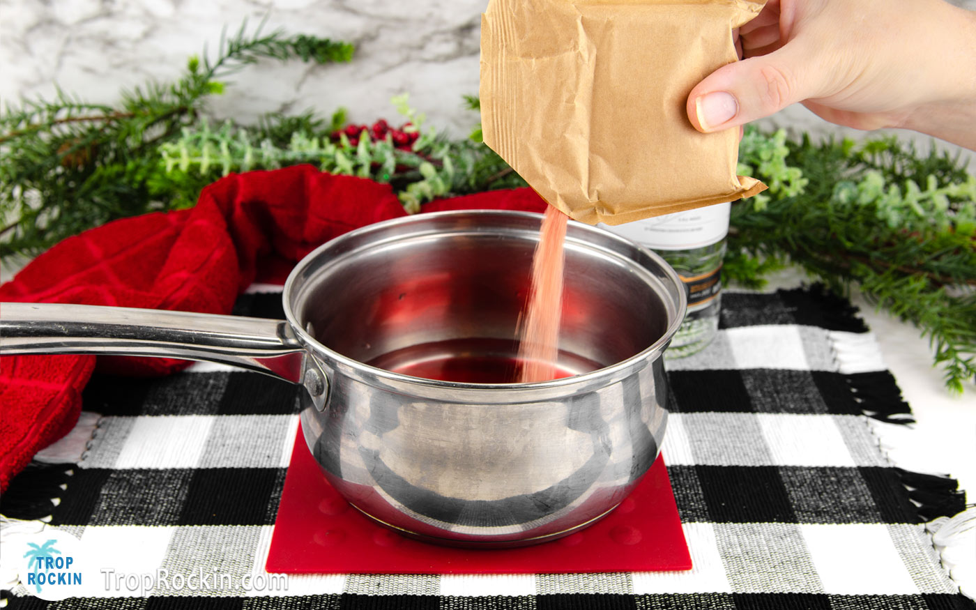 Pouring a package of jello into saucepan filled with hot water.