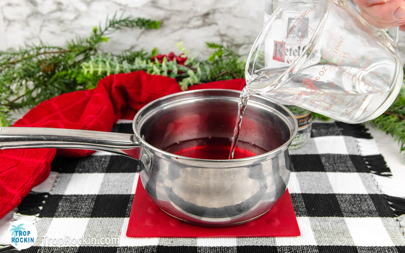 Pouring 1 cup vodka from a measuring cup into the saucepan filled with water and jello packet.