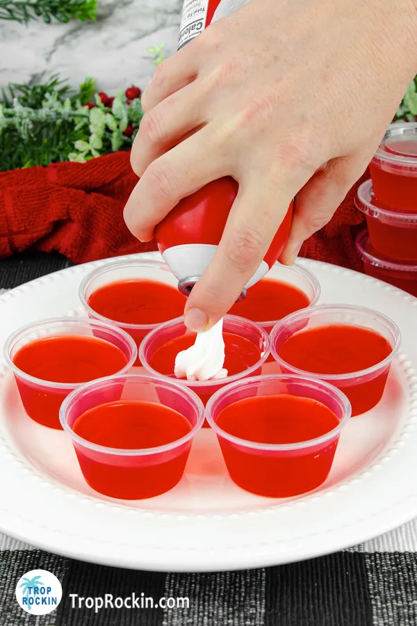 Adding redi whip whipped cream to the top of a jello shot.
