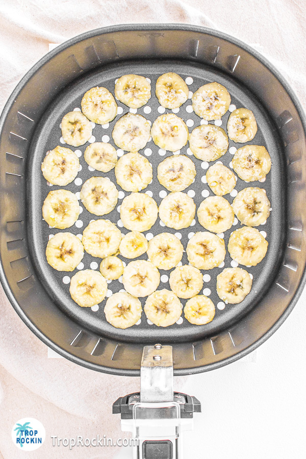 Raw banana slices evenly placed in a single layer in an air fryer basket.