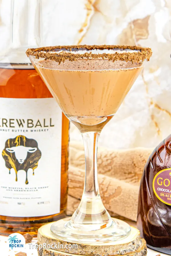 Up close view of the Peanut Butter Whiskey Martini in a martini glass with garnishes and a Skrewball whiskey bottle partly in the background.