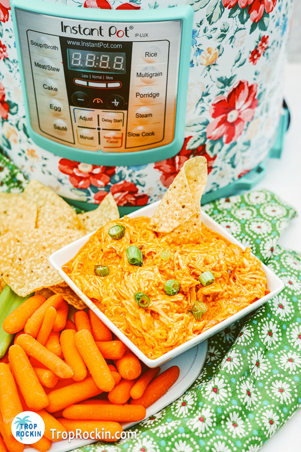 Instant Pot Buffalo Chicken Dip in a bowl with a platter of tortilla chips, celery sticks and carrot sticks with an Instant Pot in the background.