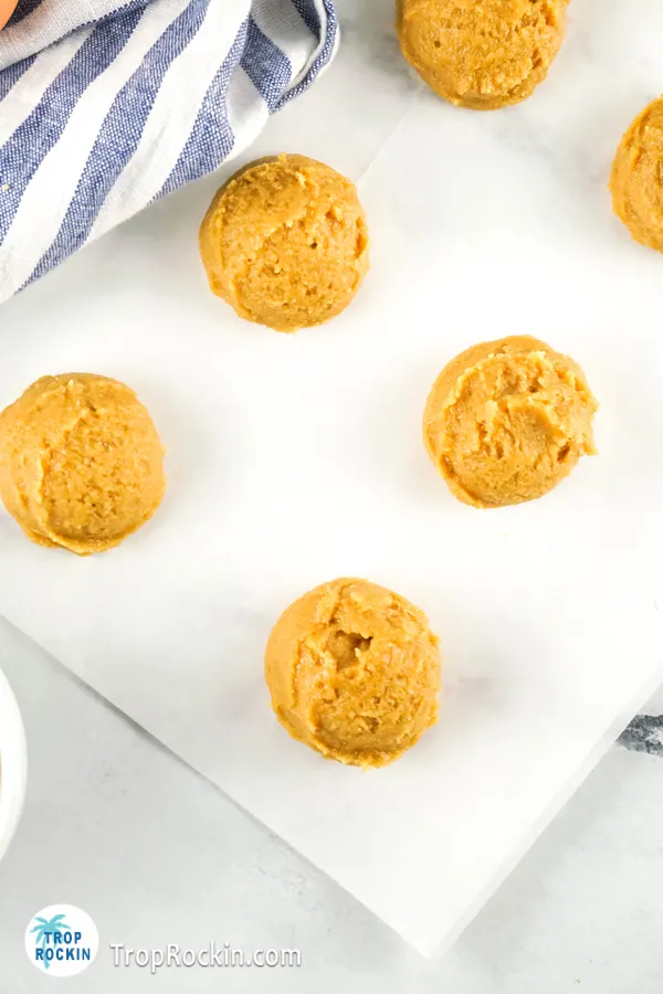 Round balls of peanut butter cookie dough on top of a piece of parchment paper.