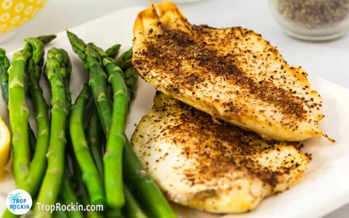 Two air fryer tilapia fillets on a white plate with asparagus on the side.