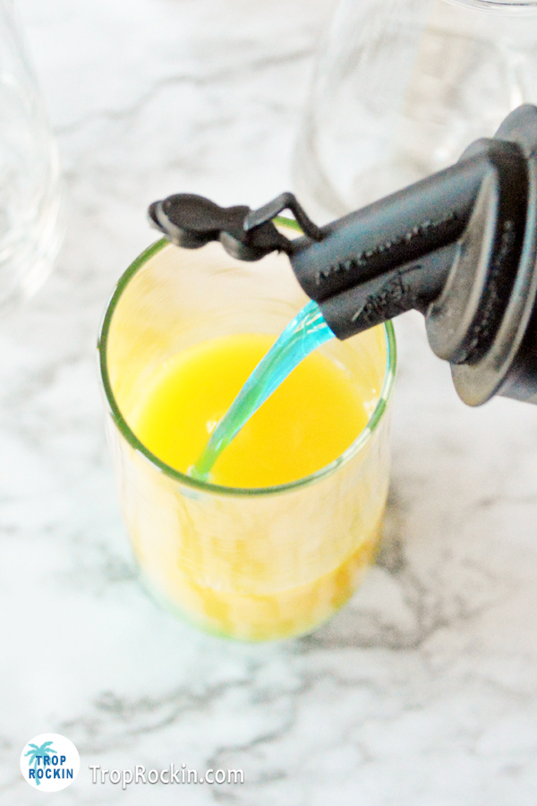 Pouring blue curacao into champagne flute with orange juice.
