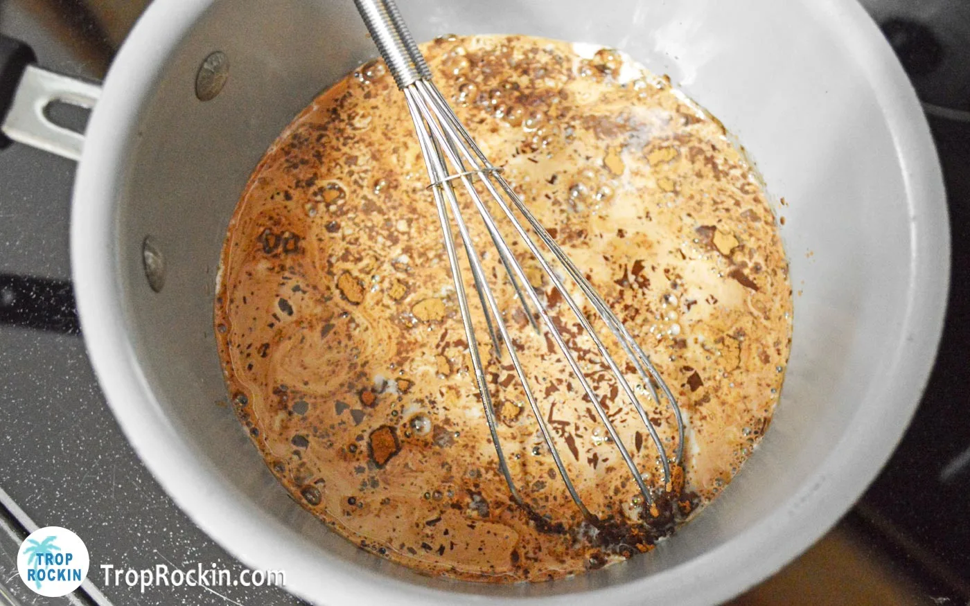 Adding chopped chocolate into the mixture in the saucepan and stiring with a whisk.