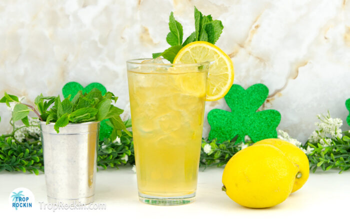 Glass of Irish Lemonade with a lemon slice and mint leaves for garnish with fresh lemons and a mint leaves in the background.