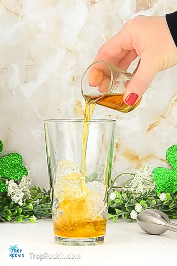Pouring a shot of irish whiskey into a glass with a few ice cubes.