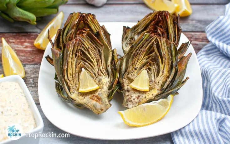Air fryer artichokes displayed on serving plate with lemon wedges.