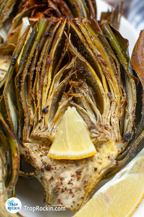 Up close view of an air fried artichoke half with a lemon wedge.