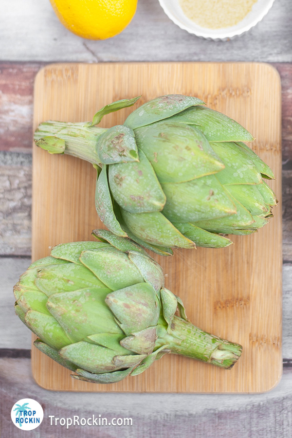 Two whole artichokes on a cutting board.