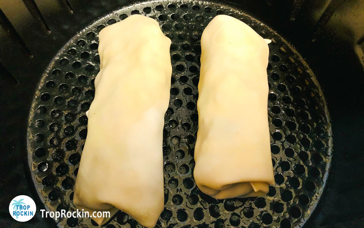 Two avocado egg rolls placed inside the air fryer basket.