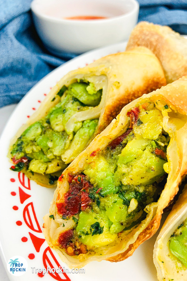 Close up of two air fryer avocado egg rolls cut in half to see the avocado filling in side.