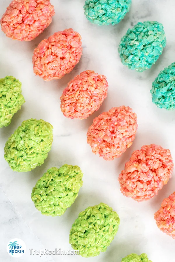 Three rows of easter egg shaped rice krispie treats. One row in blue, one in pink and the other in green displayed on a baking pan prepared with parchment paper.