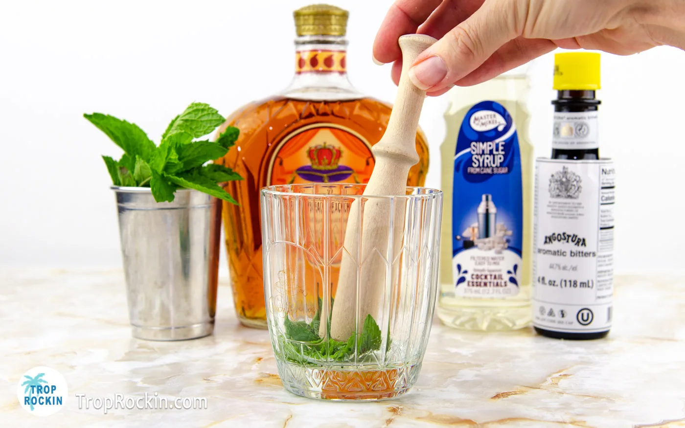Using a muddler to muddle fresh mint leaves with the simple syrup in the cocktail glass.