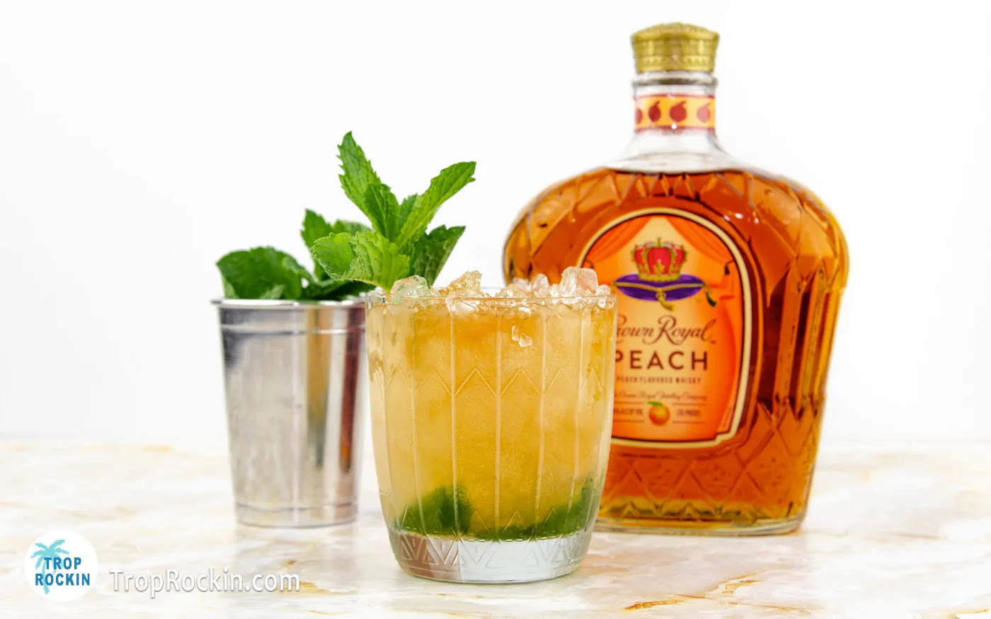 Crown Royal Peach Mint Julep with a Crown Peach bottle and cup of fresh mint in the background.