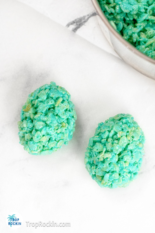 Two blue rice krispie easter eggs on a piece of parchment paper.