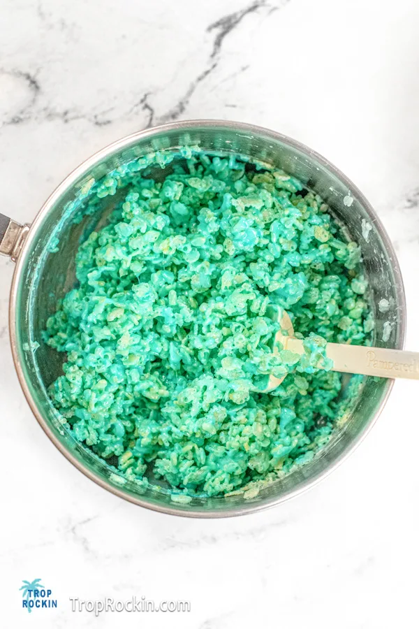 Stirring Rice Krispie cereal into the melted mixture in the pot, coloring the rice krispies blue.