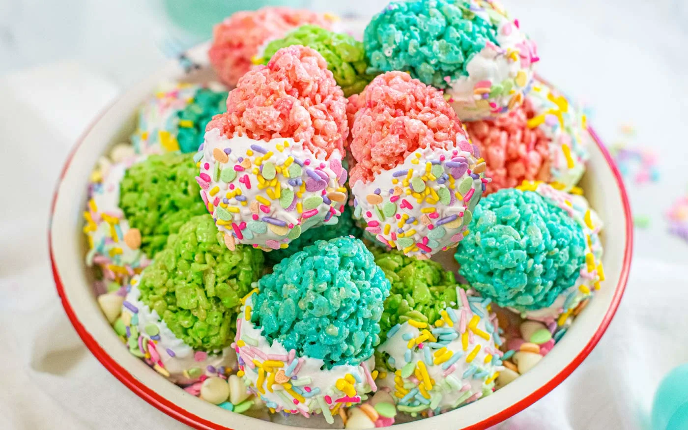 Bowl of easter egg rice krispie treats with bottom half of egg dipped in white chocolate and decorated with Easter sprinkles.