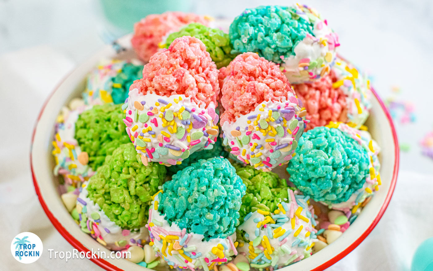 Bowl of easter egg rice krispie treats with bottom half of egg dipped in white chocolate and decorated with Easter sprinkles. 