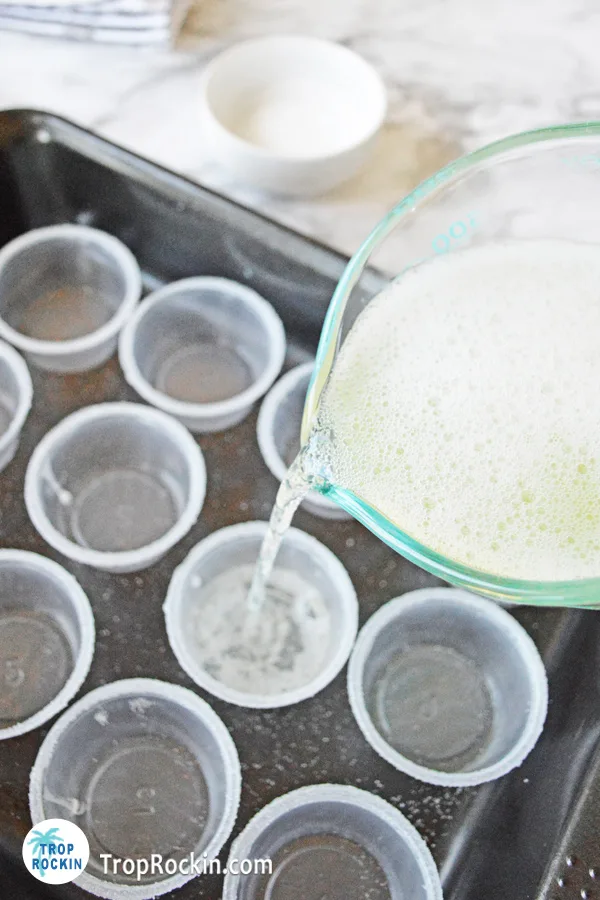 Pouring margarita tequila jello mixture into prepared mini shot glasses from a measuring cup.