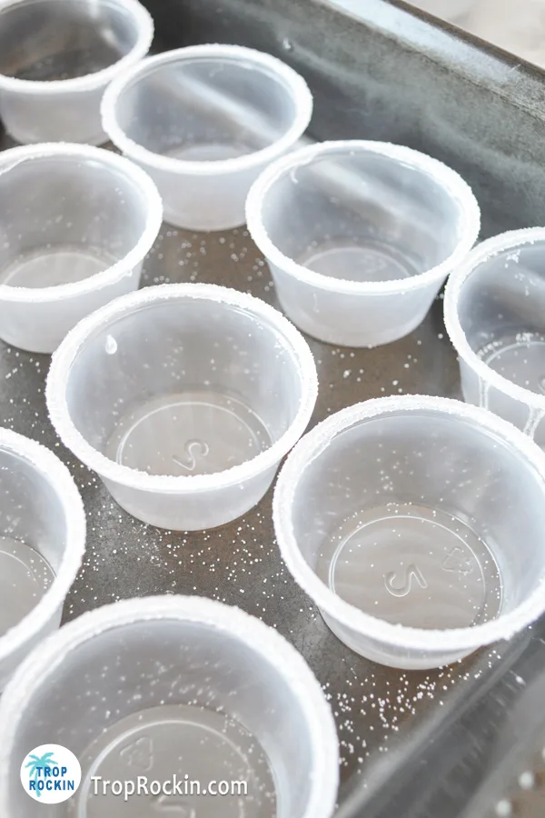 Mini plastic shot glasses with a salt rim lined up on a baking sheet.