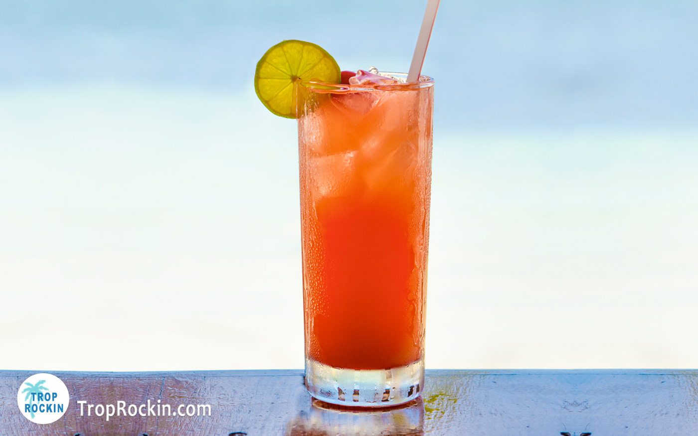 Tropical Bay Breeze drink with lime slice for garnish on table with a beach in the background.