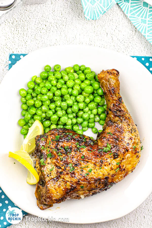 Air fried chicken leg quarter with a side of english peas on a white plate.