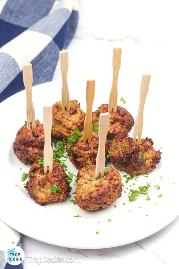 Chicken meatballs on a white plate with forked toothpicks in each one.