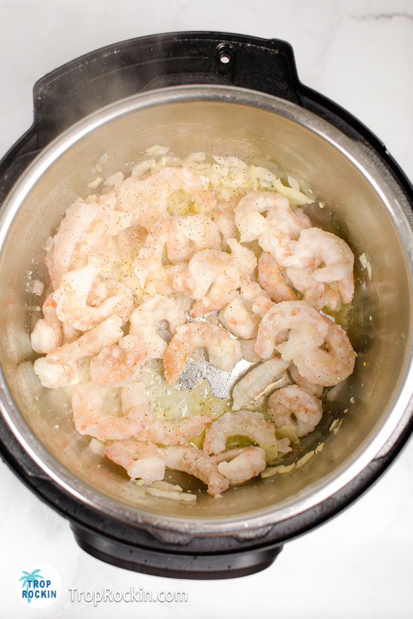 Adding shrimp to the Instant pot with sauteed onions, butter, garlic and oil.